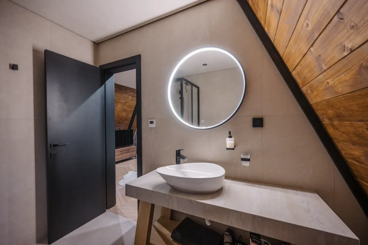 Round backlit mirror above a vessel basin set on a concrete slab, door open to the bedroom