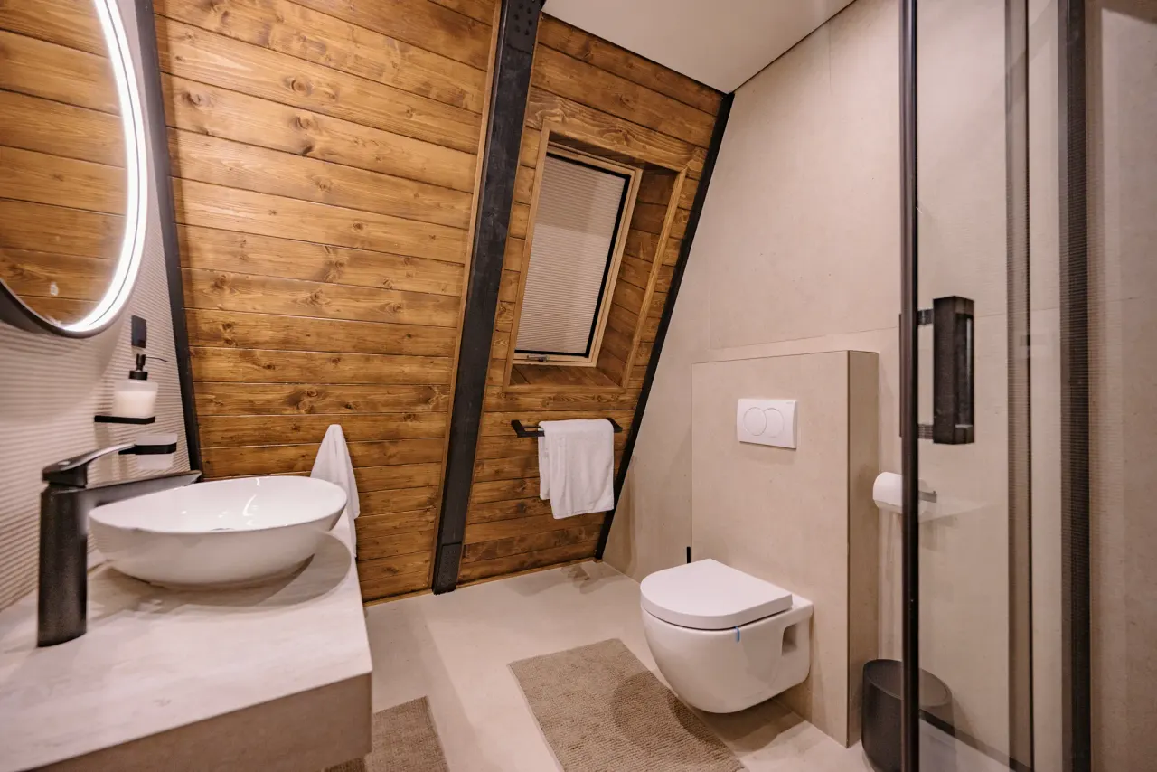 Bathroom tucked under the A-frame roof slope, timber wall behind the vessel basin