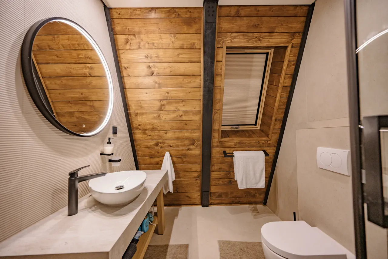 Round backlit mirror mounted on the timber-clad wall above a stone vessel basin