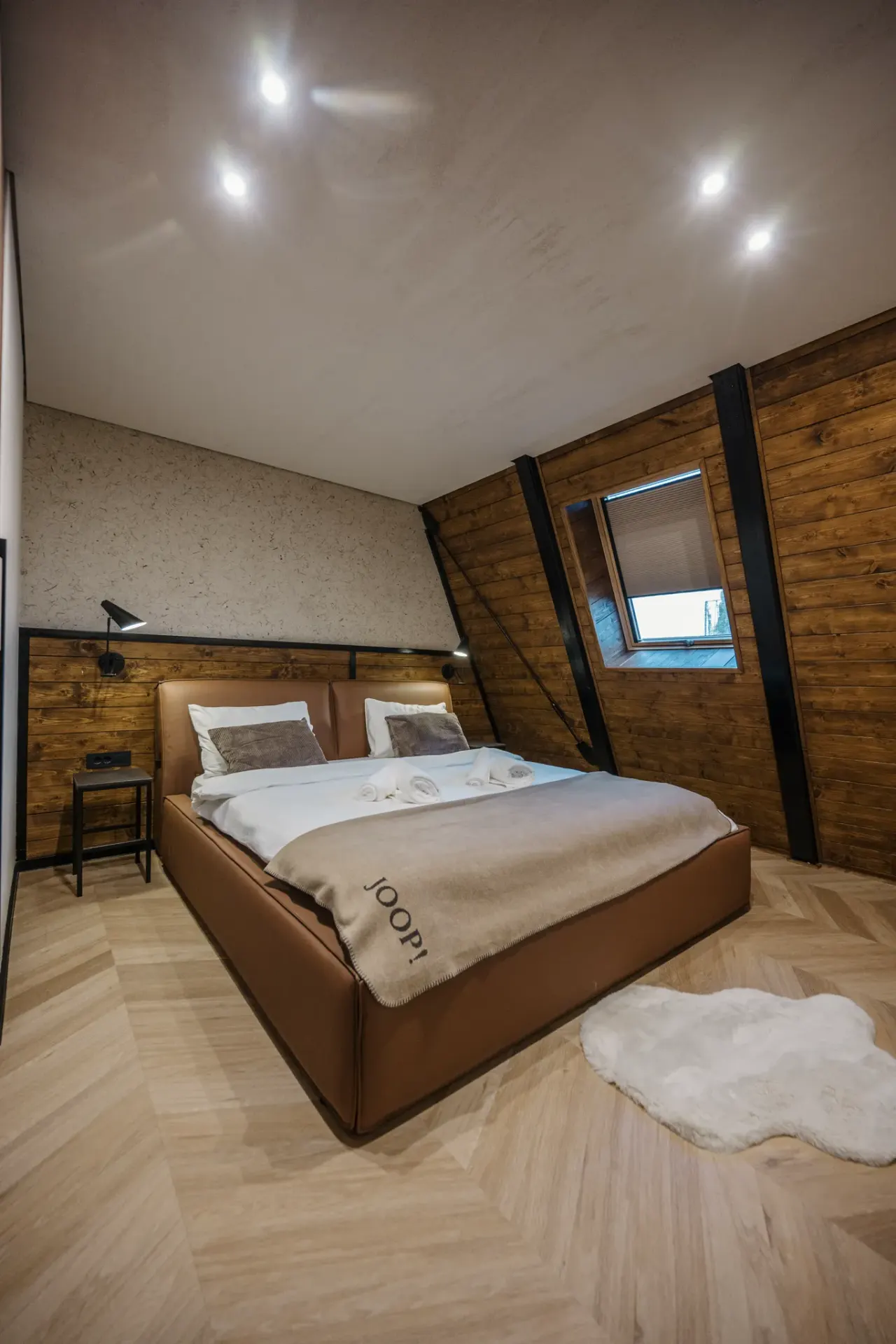 Bedroom with a cognac leather bed against a raw plaster wall and herringbone oak floor
