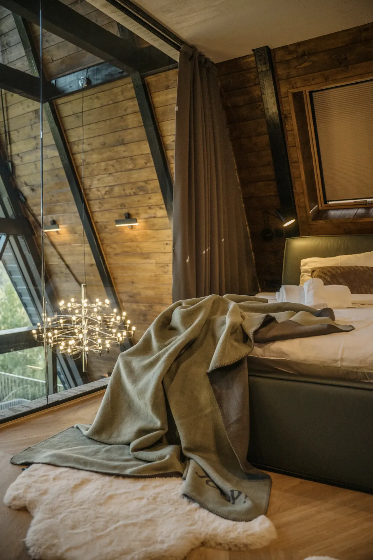 Master bedroom separated by a glass wall from the living room, the chandelier hanging beyond