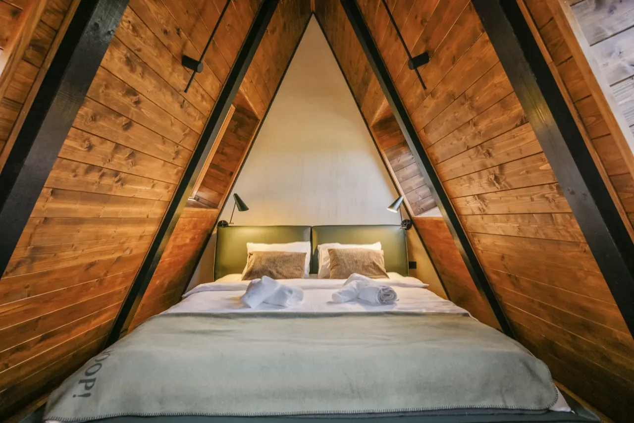 Peak bedroom bed centred under the exposed timber ridge with reading lights either side