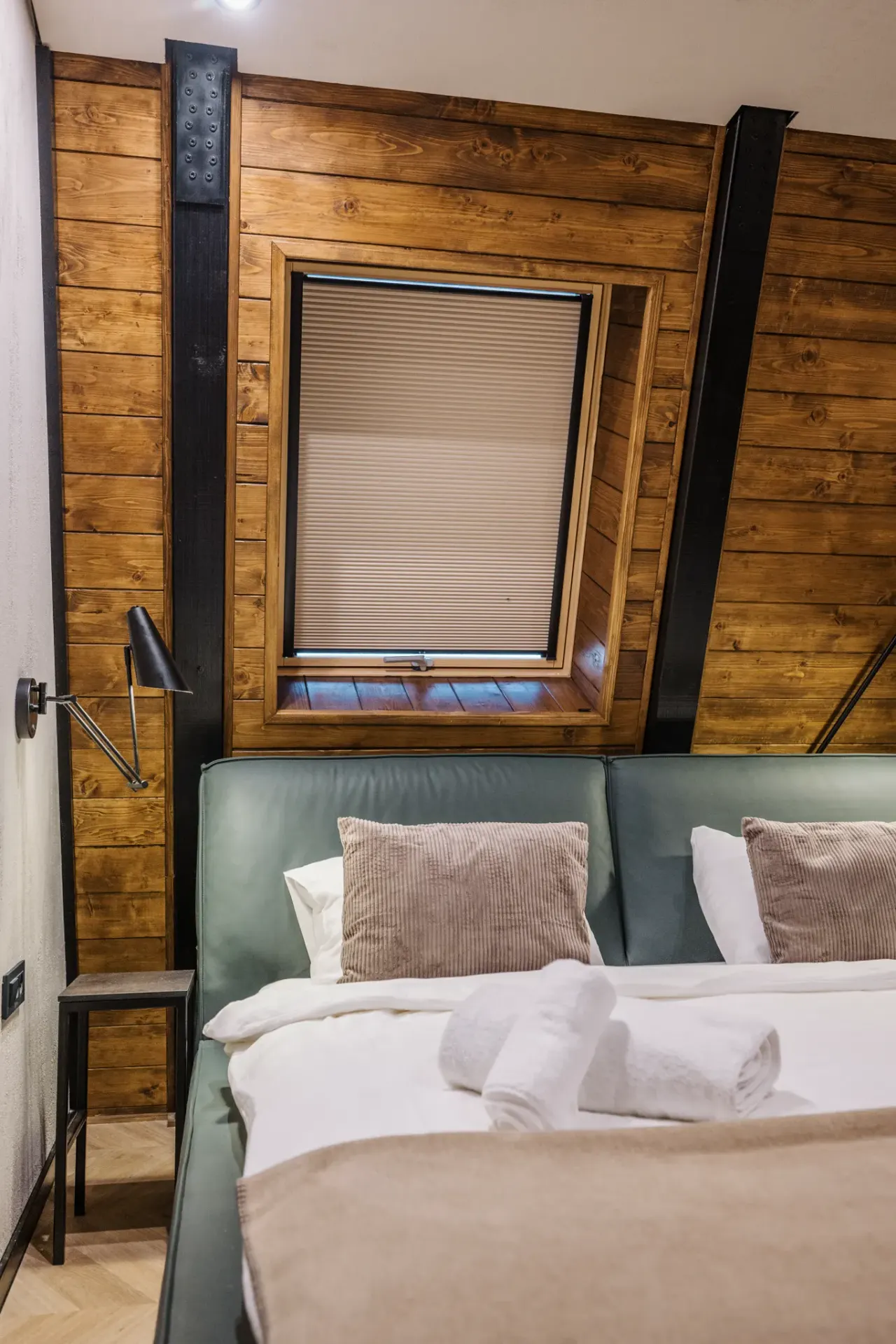 Sage-green bedroom seen head-on with the timber-framed window set into the roof slope