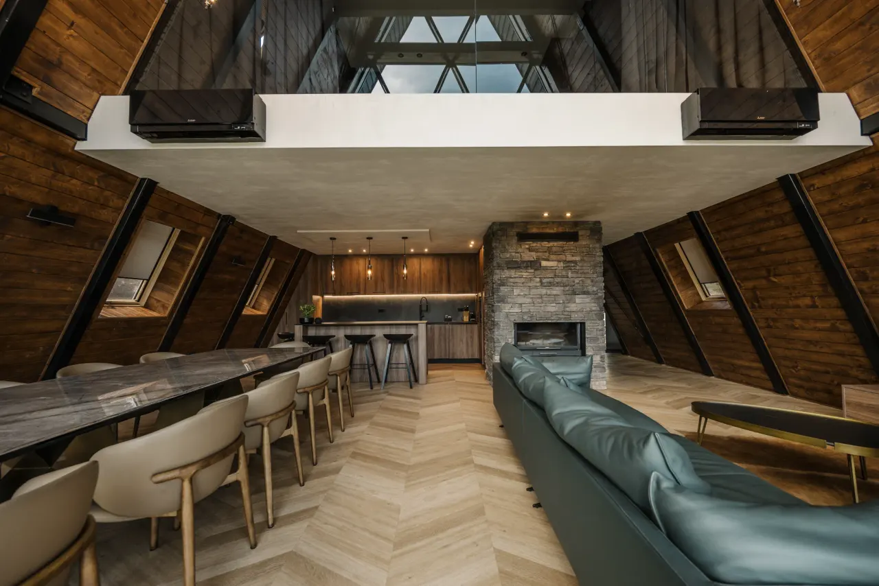 Open-plan great room with the dining table for twelve, bar stools and kitchen beyond the fireplace