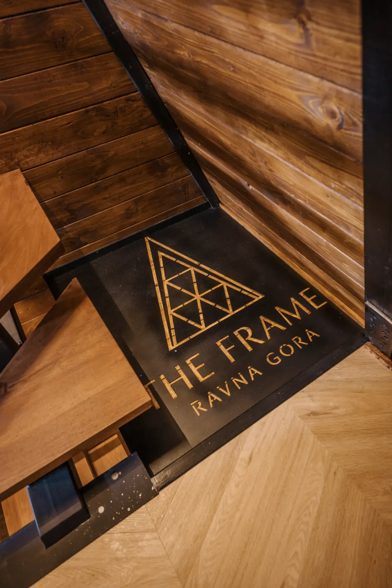 The Frame's brand mark inlaid into the oak floor at the foot of the stairs