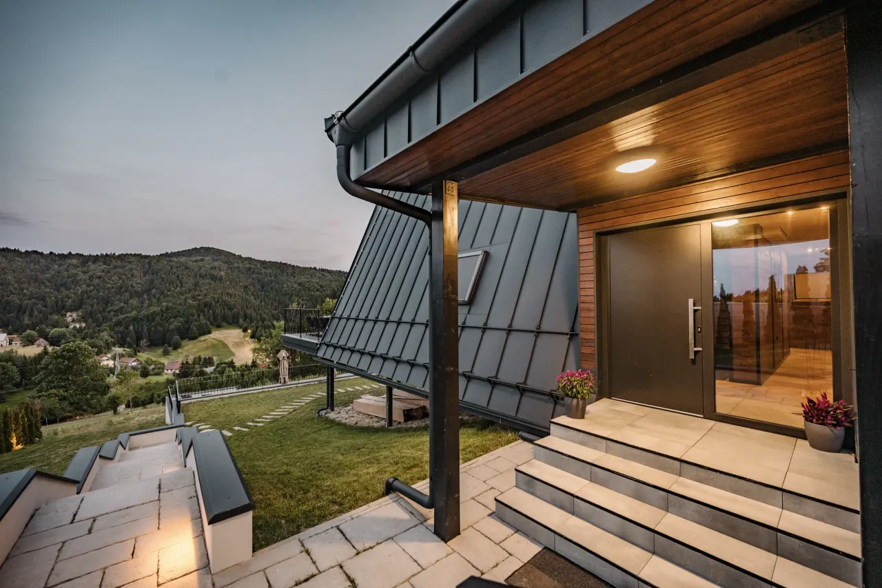 The covered entrance at dusk, warm light spilling from the timber soffit