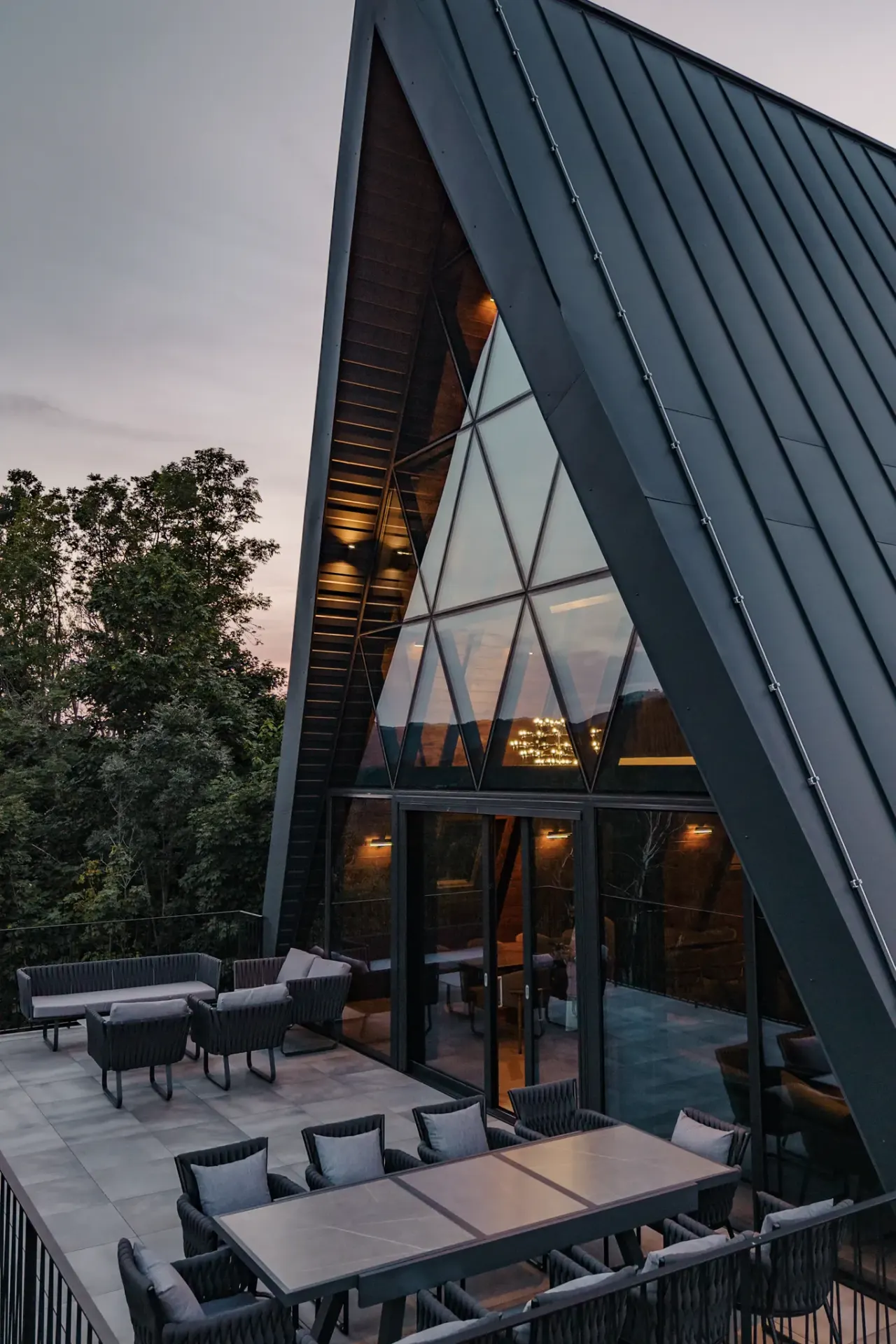 The standing-seam roof plane and triangular glass gable of the A-frame above the terrace at last light