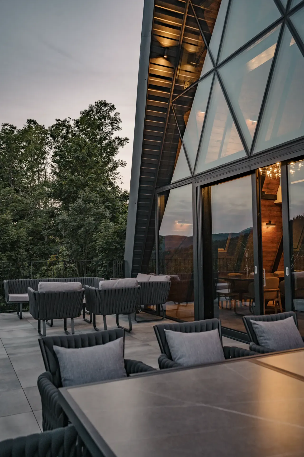 The glass wall and terrace at last light, the forest edge falling away beyond the railing