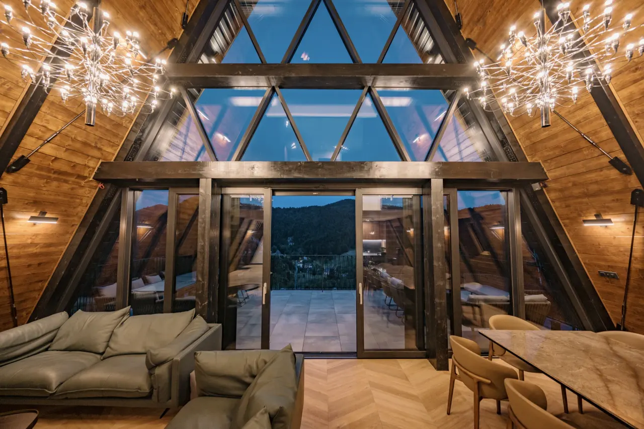Living room at dusk with chandeliers and the glass gable against a twilight sky