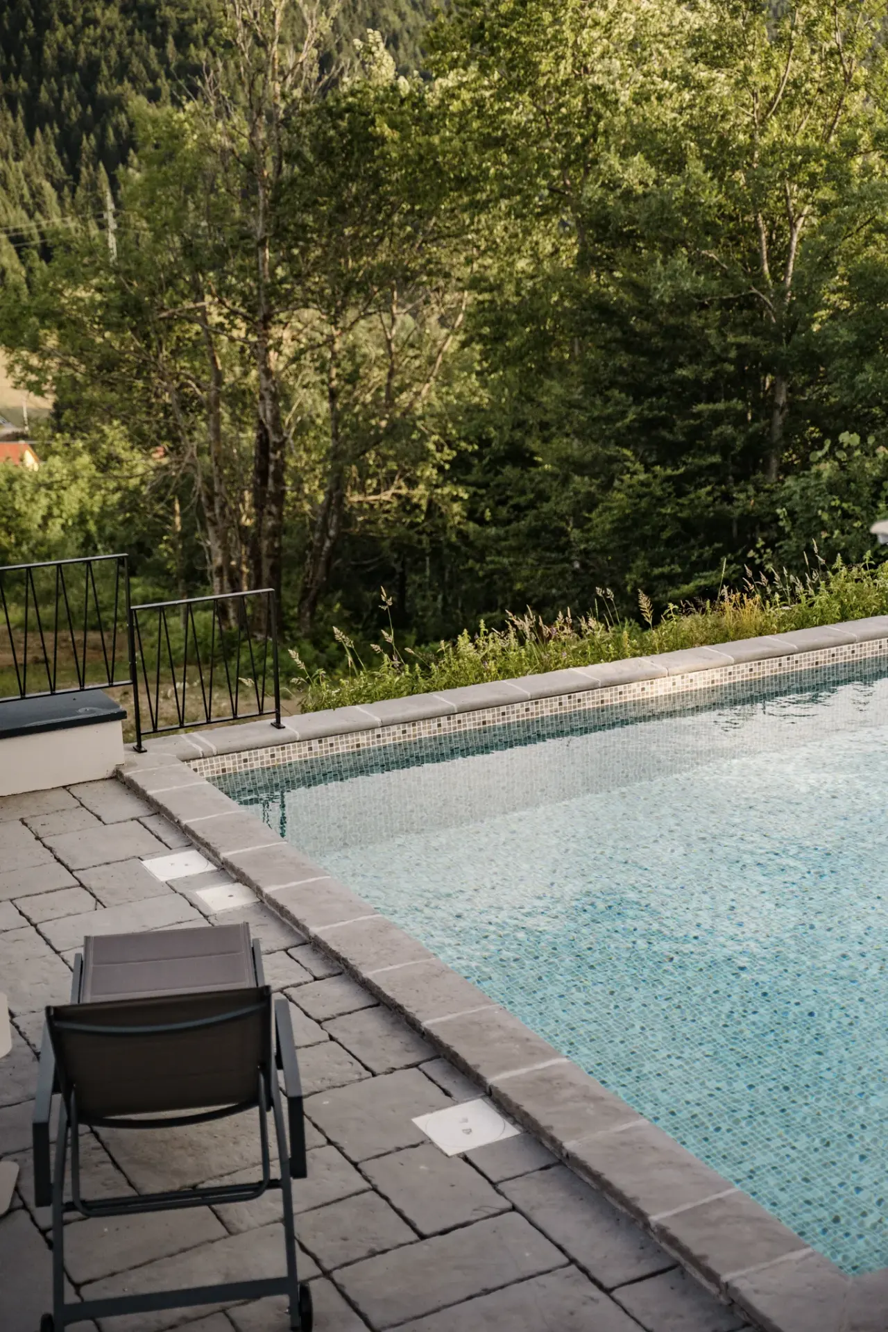 Still water at the pool edge with a lounger and the treeline behind