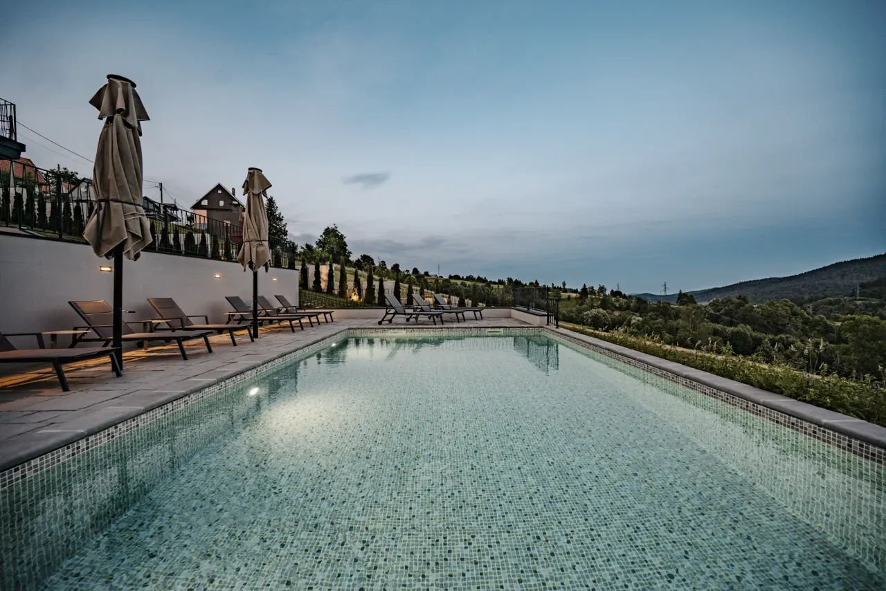 The heated pool lit turquoise at dusk, loungers and parasols along its edge