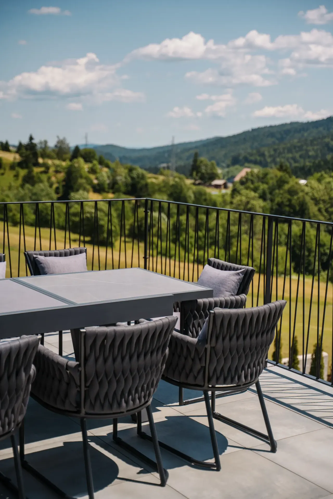 Outdoor dining table and woven armchairs on the terrace above the forested hills