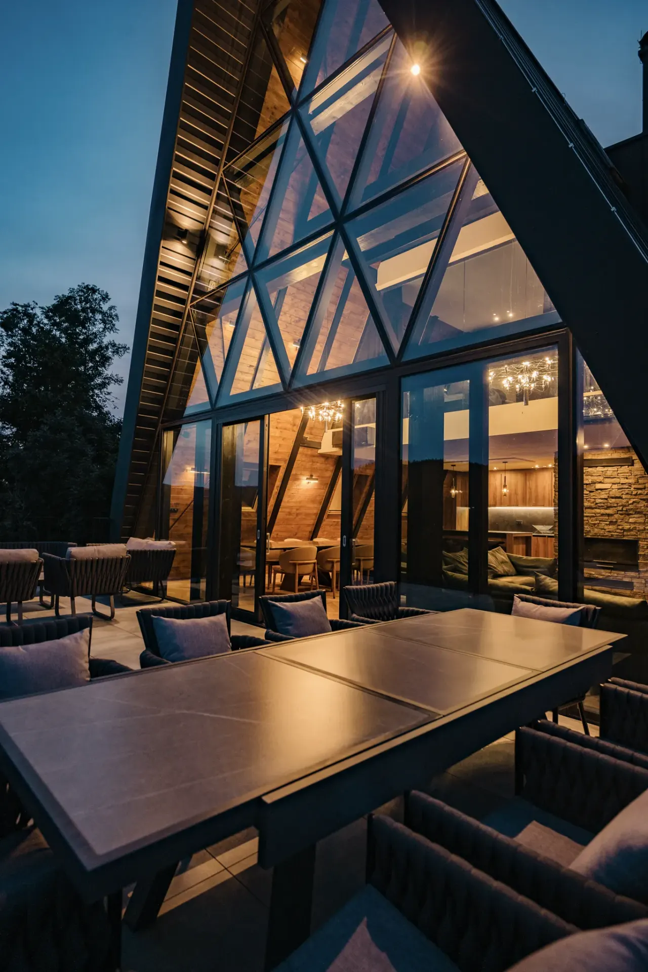 The terrace dining table at dusk with the glass facade lit from inside