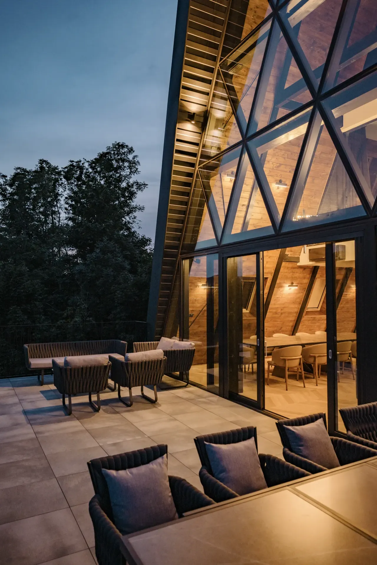 Terrace lounge chairs in the evening beside the illuminated A-frame facade