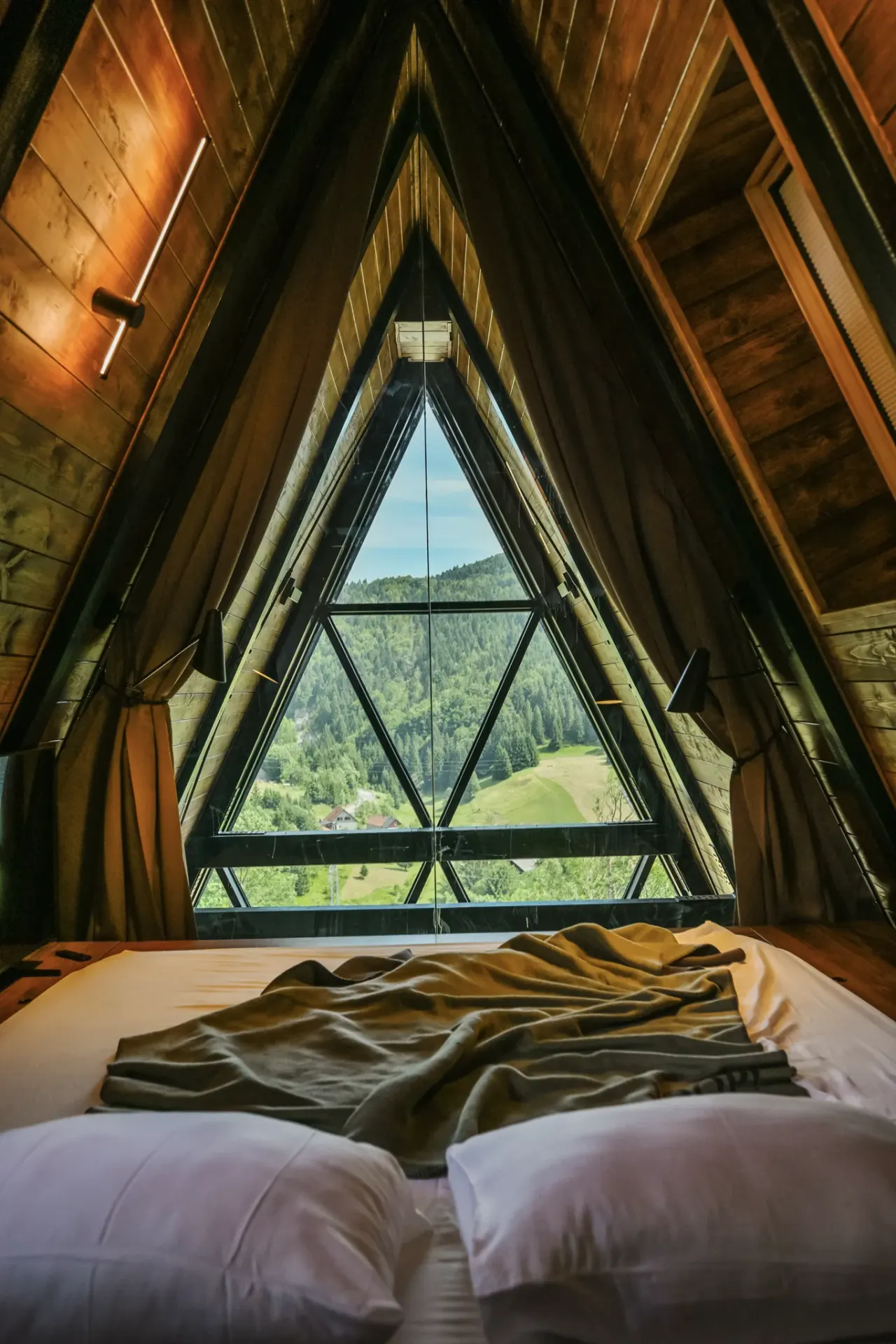 Bedroom framed by the triangular A-frame glass gable over the forest