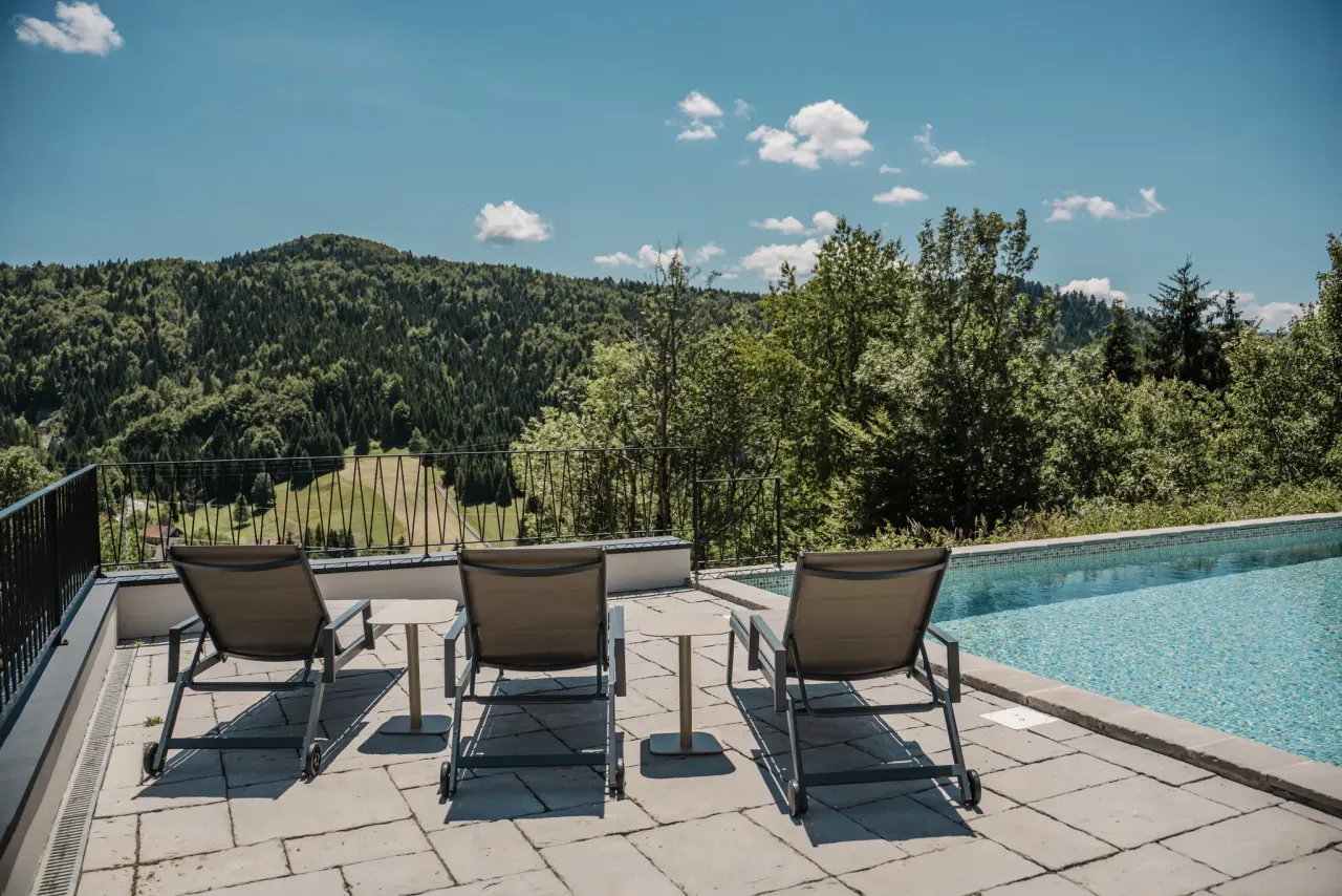 Sun loungers and a side table facing the pool and the forested hills beyond