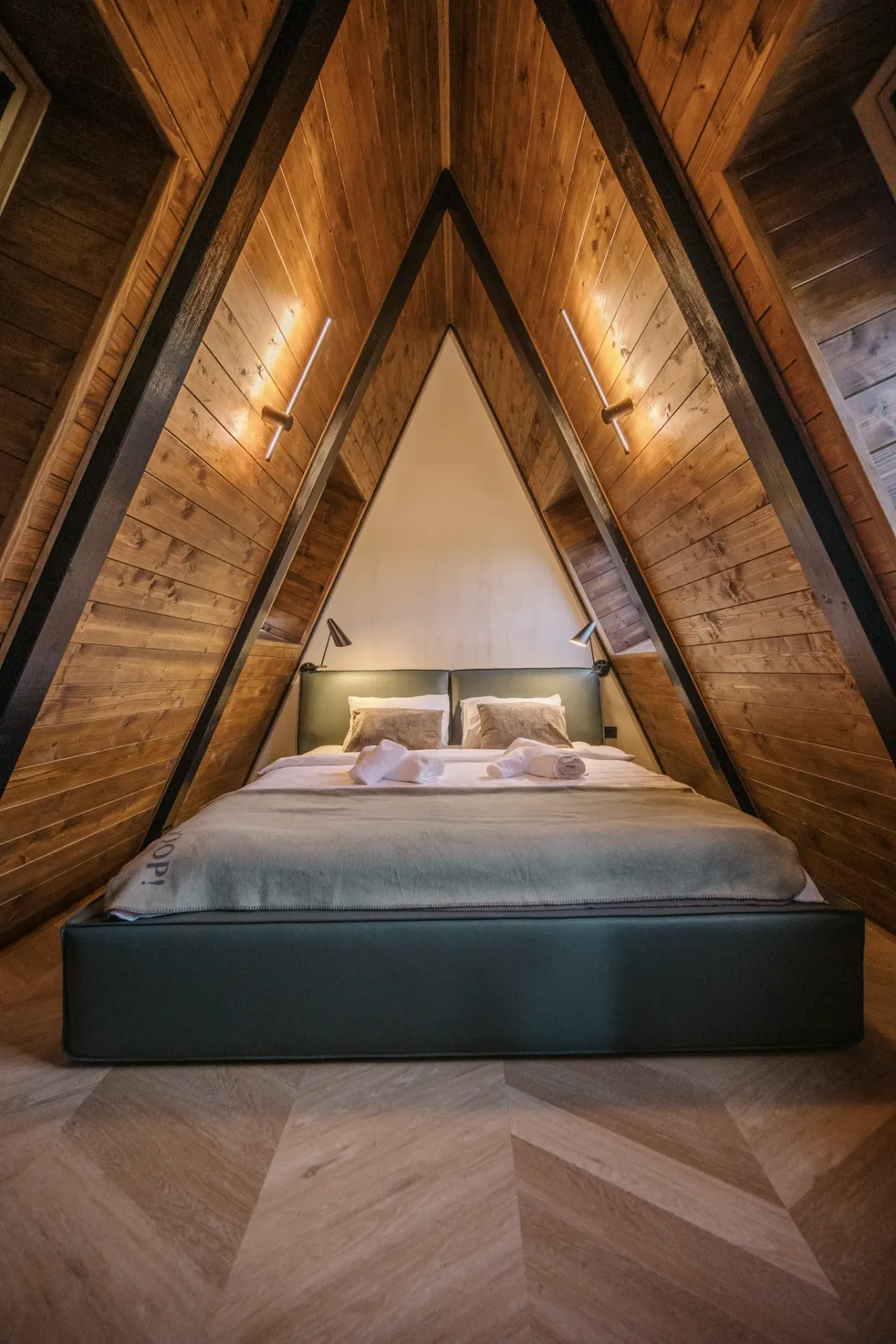 Attic bedroom tucked under the timber A-frame apex, framed by a triangular gable
