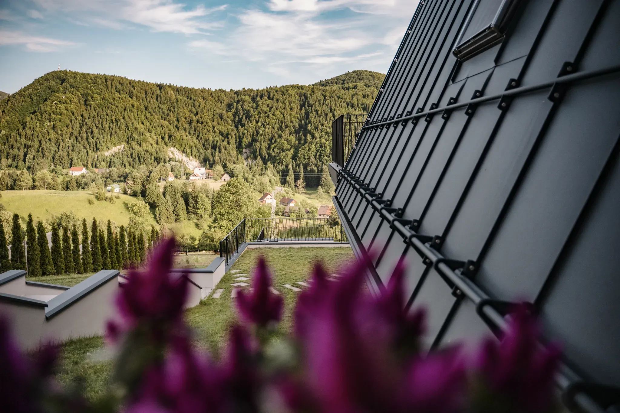 Wildflowers in bloom against the standing-seam facade of the A-frame on Ravna Gora