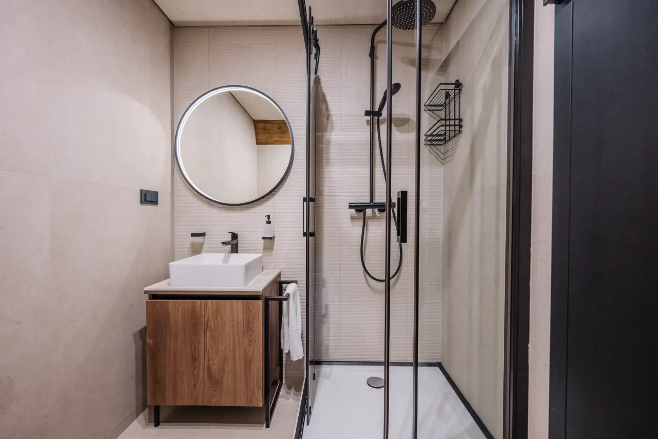 Bathroom with a round mirror, walk-in glass shower and timber vanity